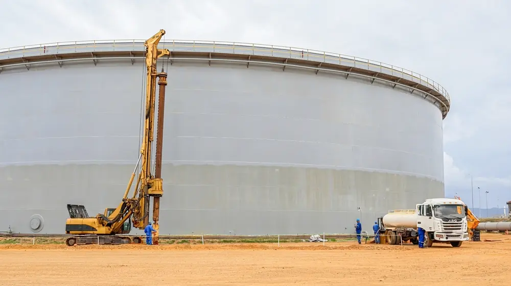 Equipo de perforación trabajando junto a un tanque de almacenamiento