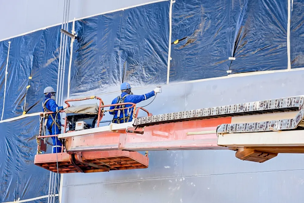 Operarios pintando la pared del tanque desde plataforma elevadora