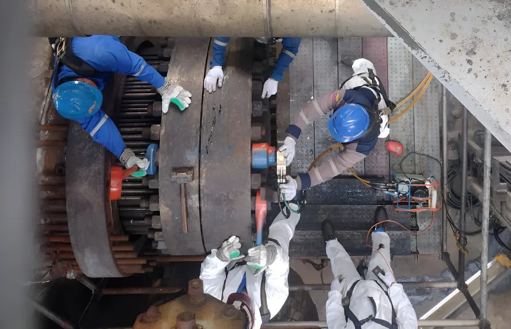 Cuadrilla con trajes de protección abriendo la brida de un intercambiador de calor